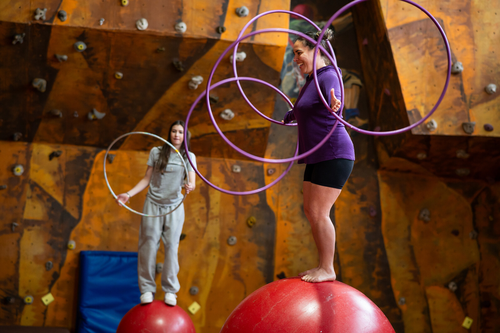 2.	A young girl holding a hula-hoop watches a smiling woman play with a purple hula-hoop 