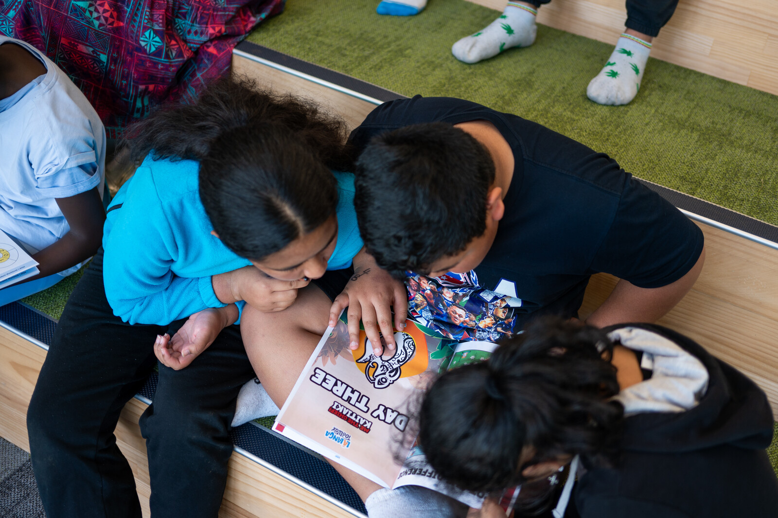 A birds eye view of three young students sitting on the bleachers engrossed in a workbook