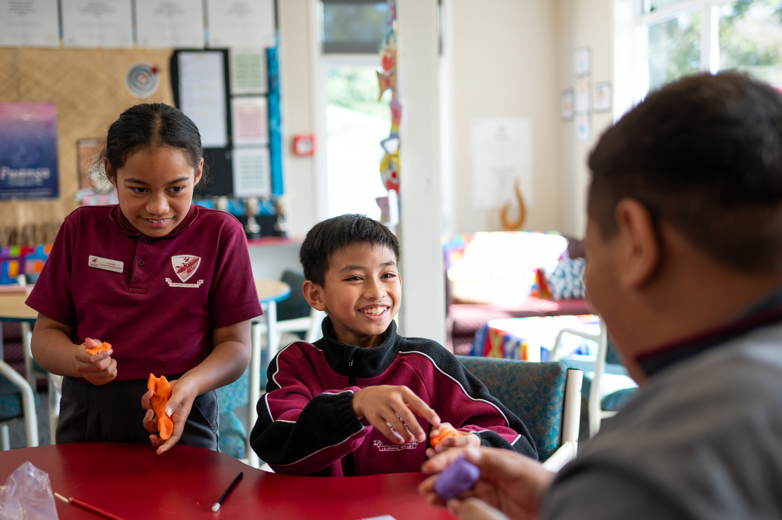Two children in their school uniforms smile as they play with colourful play-dough 