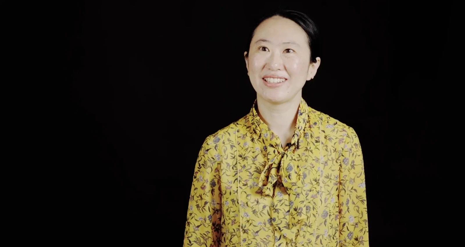 A Te Pūaha Talks attendee in a yellow floral top smiles warmly at the camera.