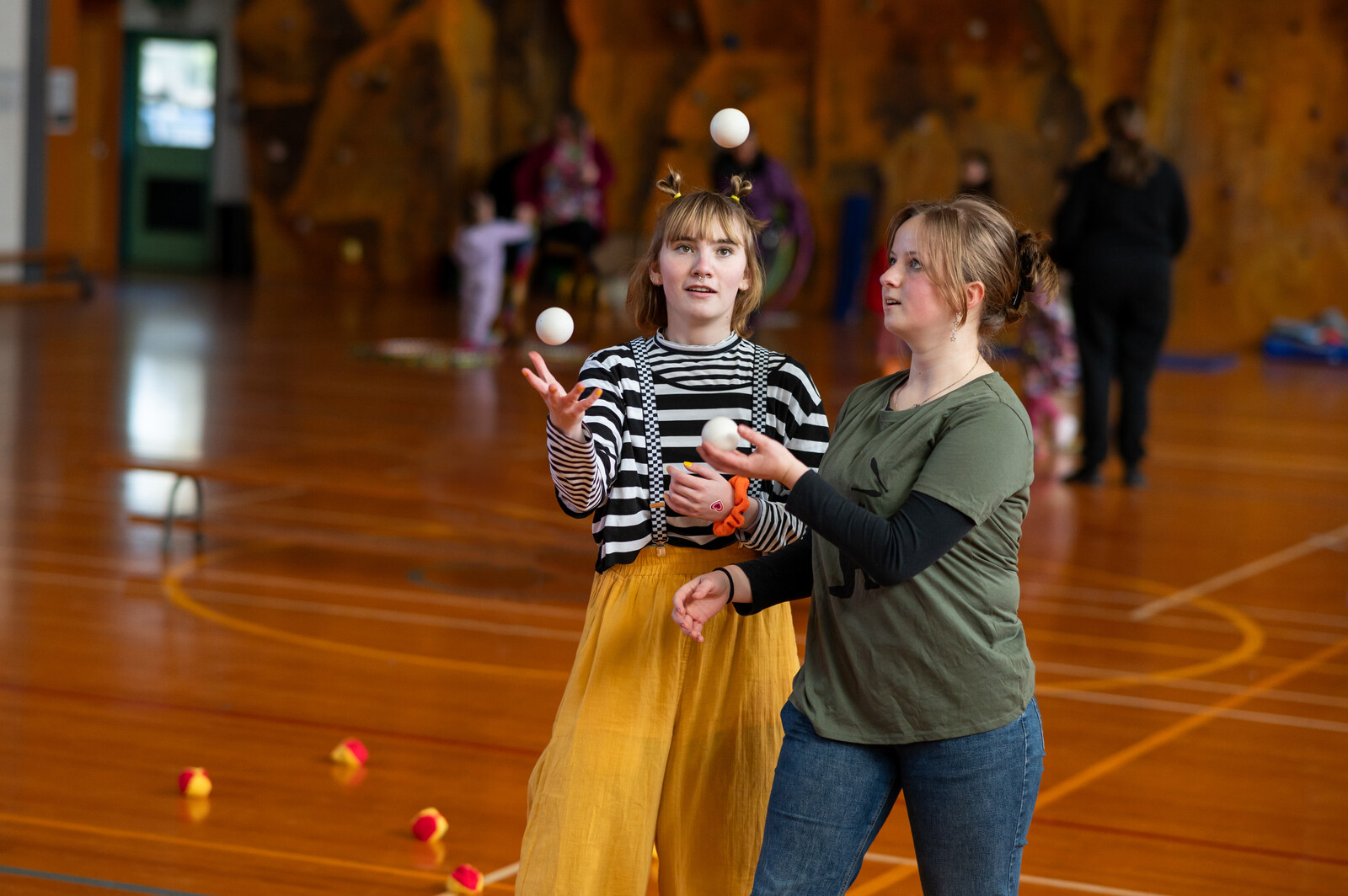 Two girls stand together juggling inside a school gym 