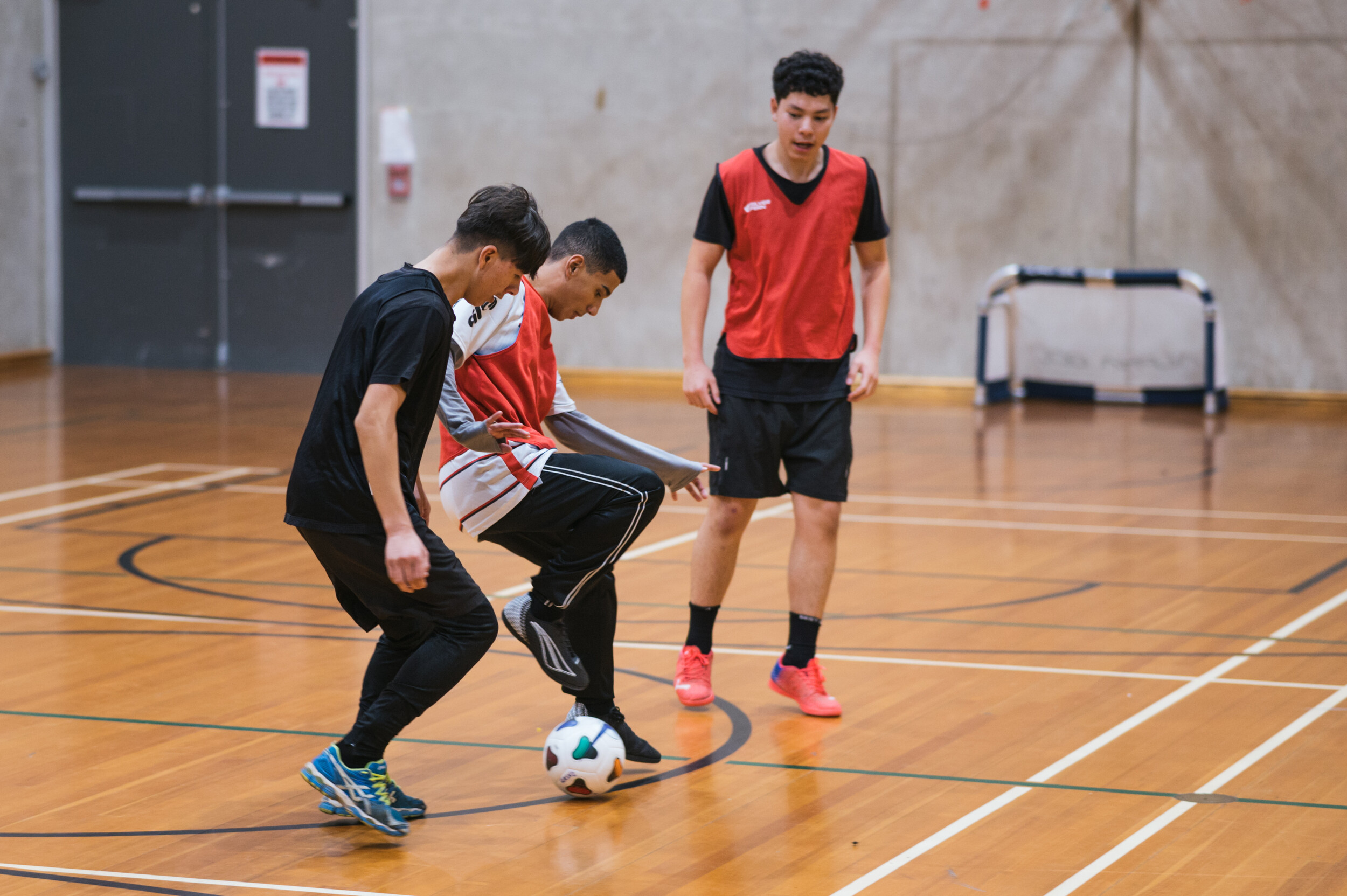 A group of young men play football on an indoor basketball court