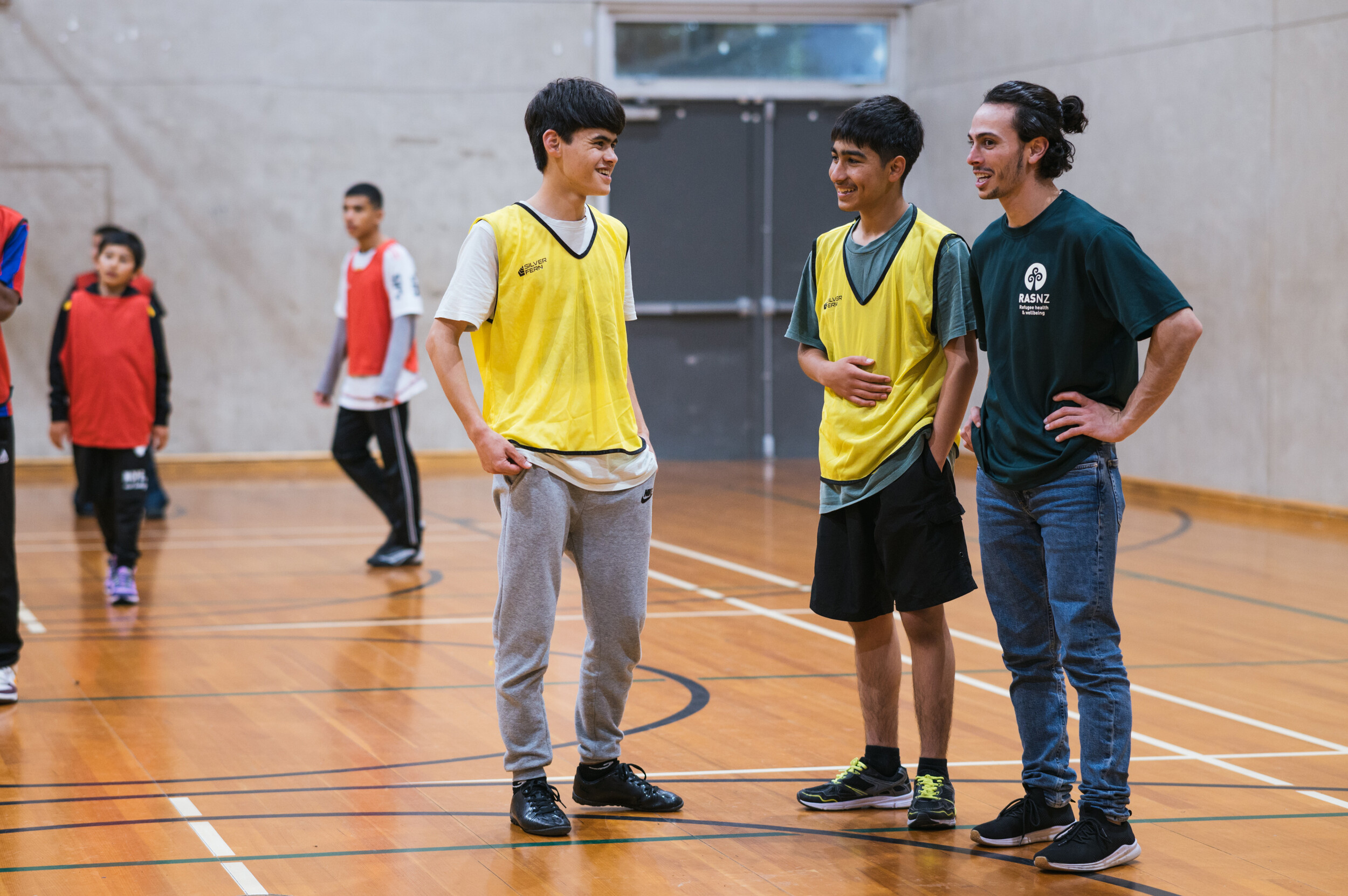 1.	Three young men standing on an indoor basketball court smile and talk to each other 